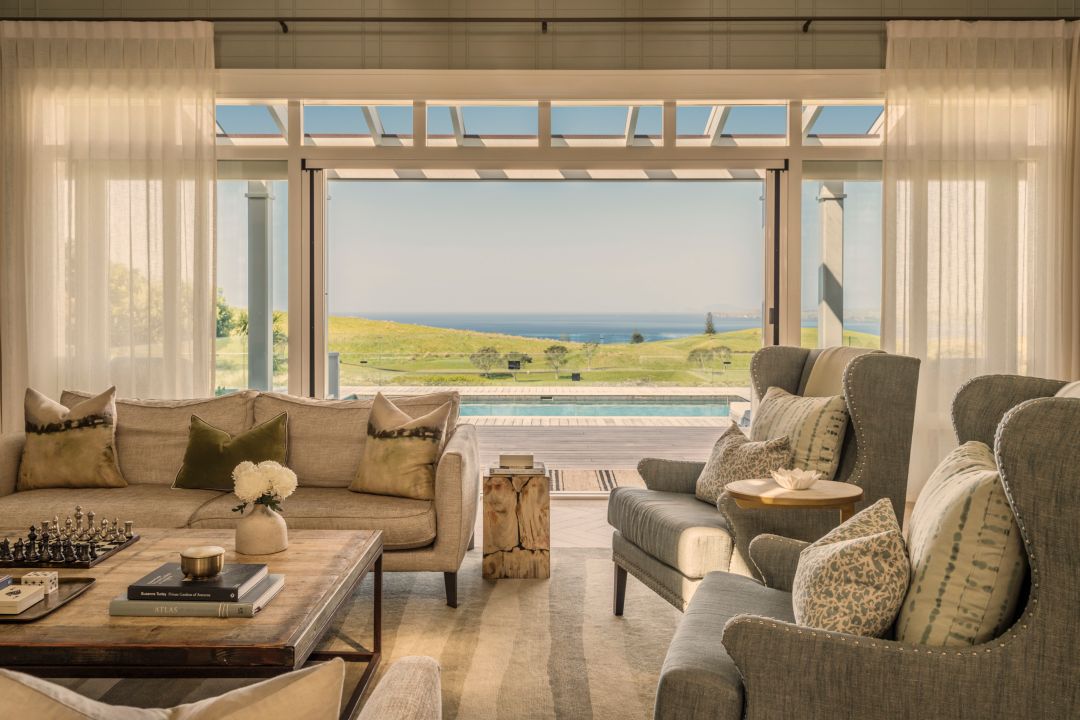 Living room in a luxury four bedroom villa with timeless furnishings, sheer curtains and open doors leading out the covered terrace and pool.
